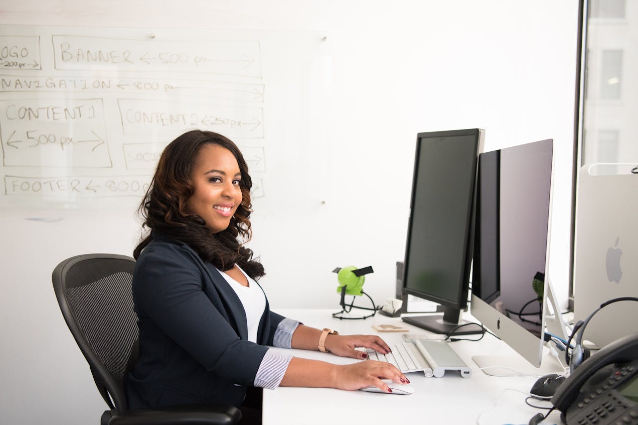 Confident businesswoman seated at her desk in an office, typing on a computer.